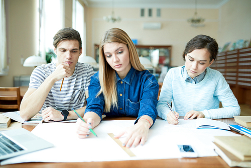 Serious puzzled engineering students looking at sketch and discussing it while planning their construction project in library