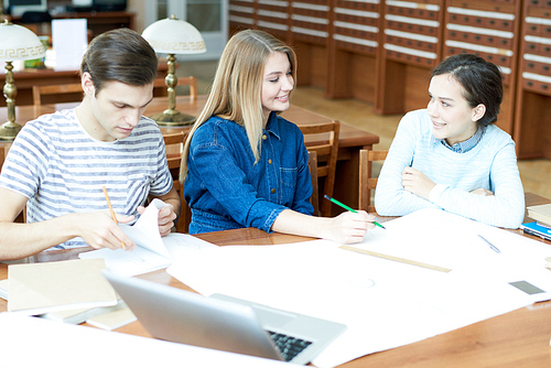 Group of positive optimistic friends drawing sketch together discussing classes in library after university and sitting at table with blueprint