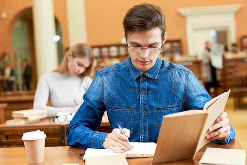 Serious busy smart student boy summarizing information from textbook while studying in comfortable library and concentrated on homework