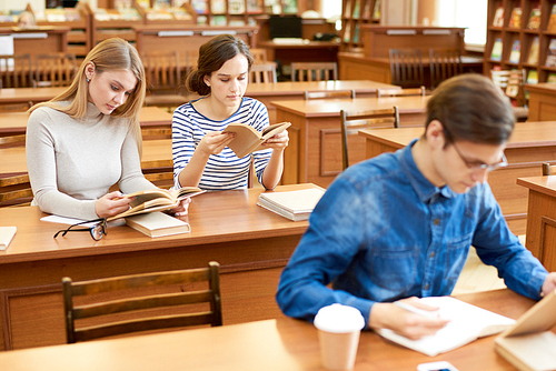 Serious concentrated college students using library resources while making research or preparing for exam