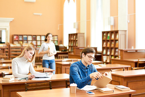 Busy concentrated students sitting at wooden tables and studying scientific publications and summarizing information in modern library