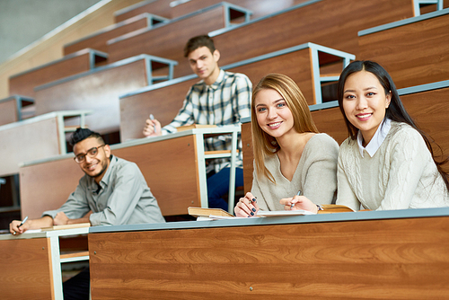 Multi-ethnic  group of people sitting at separate tables in lecture hall of modern college, focus on two beautiful girls  and smiling, copy space