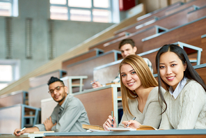 Multi-ethnic group of students sitting at tables in lecture hall of modern college, focus on two beautiful girls  and smiling, copy space