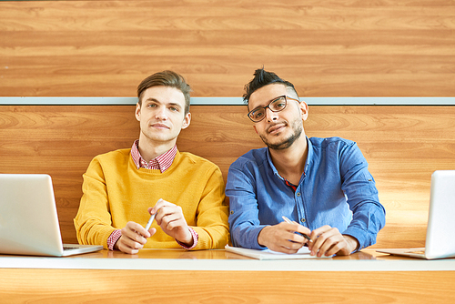 Portrait of two students sitting at desk in modern auditorium at college and , one of them Middle-Eastern