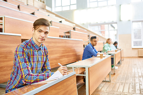 International group of people sitting in row at  tables in lecture hall of modern college, focus on smart young man in foreground, copy space