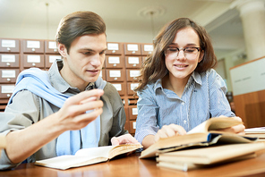 Positive satisfied school student friends analyzing textbook contain while working on scientific project together in library