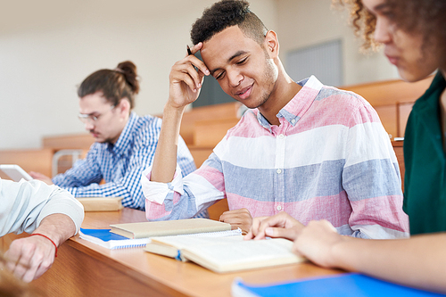 Afroamerican student sitting at desk and studying together with his classmates