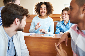 Cheerful excited pretty African-American student girl gesturing while explaining idea for university project to groupmates while they brainstorming in lecture room