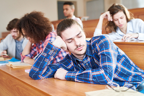 Young man sitting at desk and sleeping during a lesson at college