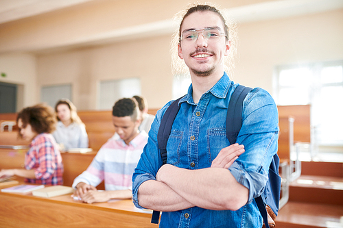 Portrait of smiling student in eyeglasses standing at classroom