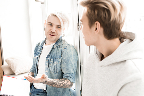 Caucasian adult student with tattooed hands and dyed blond hair discussing assignment with his young college mate