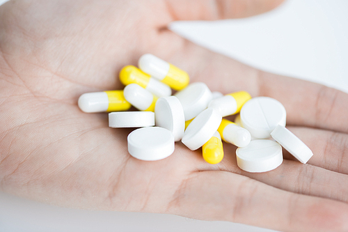 Closeup of hand holding several pills and drugs for treatment of illness over white background