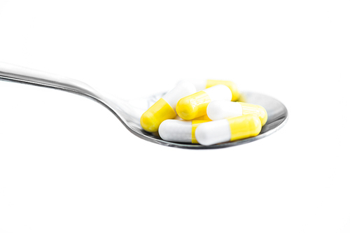 Side view closeup of spoonful of yellow capsules isolated on white, medicine concept, copy space