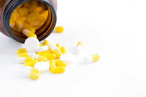 Closeup of assorted medication capsules spilling from bottle over white background, copy space