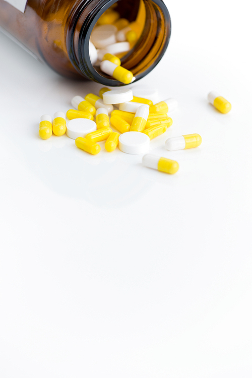 Close up of assorted medication capsules spilling from bottle over white background, copy space