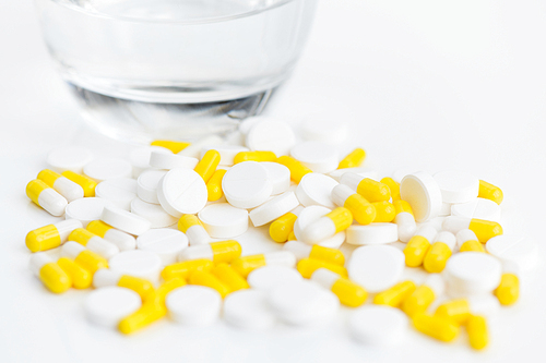 Closeup of assorted pills and drugs on white background next to glass of water, medicine and treatment concept