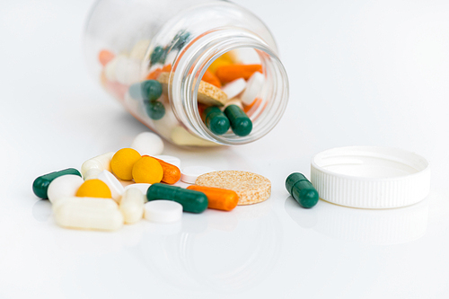 Close up of assorted colorful medication drugs and vitamins spilling from bottle over white background