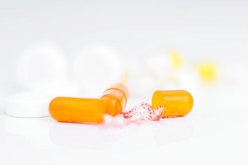 Close up shot of opened gelatin capsule with drug substance spilling on white background, medication concept