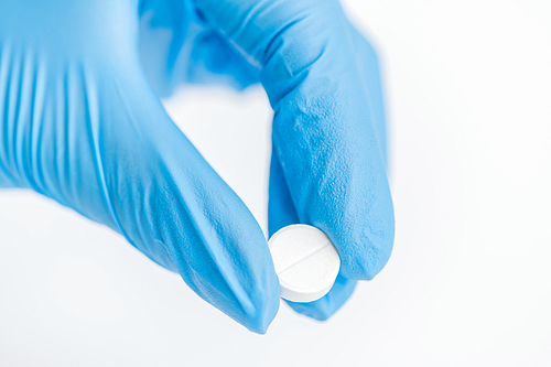 Closeup of gloved hand holding single white pill over white background, medicine and treatment concept