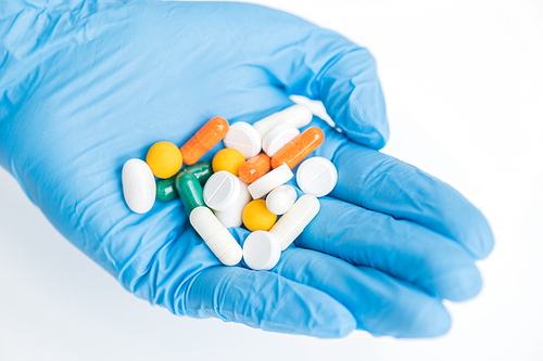 Closeup of gloved hand holding assorted pills over white background, medicine and treatment concept