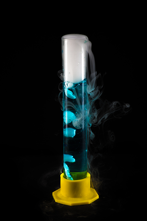Closeup of steaming test tube with blue liquid against black background, chemical experiment concept