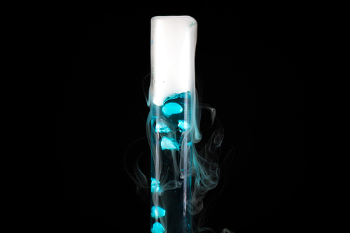 Close up of test tube with blue liquid with cold steam pouring from it against black background, chemical experiment concept