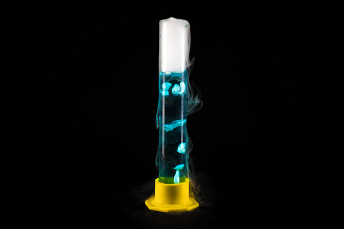 Close up of glass tube with blue liquid with cold steam pouring from it against black background, chemical experiment concept