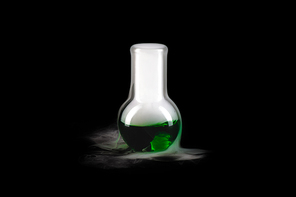Close up of glass flask with green steaming liquid on black background, copy space