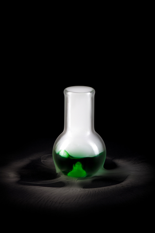 Closeup of glass flask with green liquid  and steam pouring from it on black background, copy space