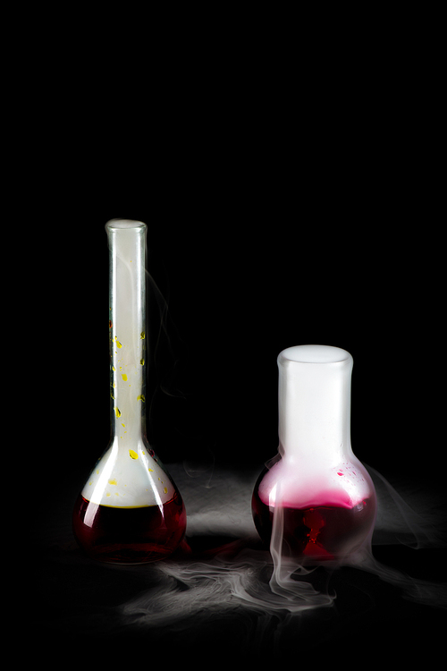 Closeup of two glass flasks with red liquid  and steam pouring from it on black background, copy space