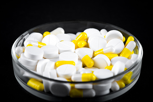 Closeup of assorted pills in petri dish on black background, pharmaceutical industry concept