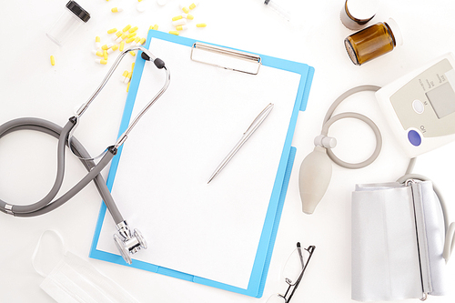 Top view flatlay of doctors tools on white desk composition of stethoscope and  clipboard, glasses and blood pressure monitor, copy space