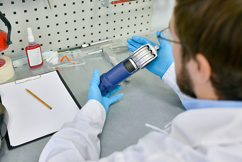 High angle view of young prosthetics technician holding prosthetic leg part at desk in office, checking it for quality and making adjustments