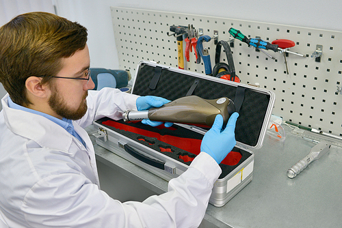 Portrait of young medical engineer examining case with prosthetic equipment at desk in office, checking it for quality and packing it