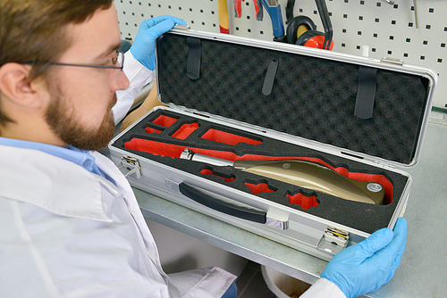 High angle view of young  prosthetics technician holding case with prosthetic equipment at desk in office, checking it for quality and packing it