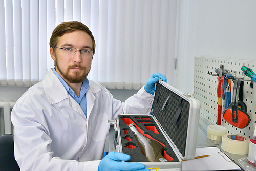 Portrait of  medical engineer holding case with prosthetic leg and  posing in laboratory