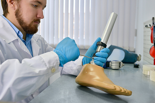 Side view of  prosthetist repairing  prosthetic leg part at desk in office, checking it for quality and making adjustments