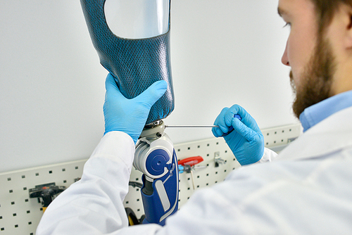 Portrait of prosthetics technician making leg prosthesis sitting at desk in modern laboratory, checking it for quality and making adjustments