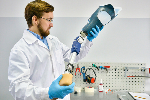 Portrait of young  prosthetics technician holding prosthetic leg  checking it for quality and making adjustments while working in modern laboratory, copy space