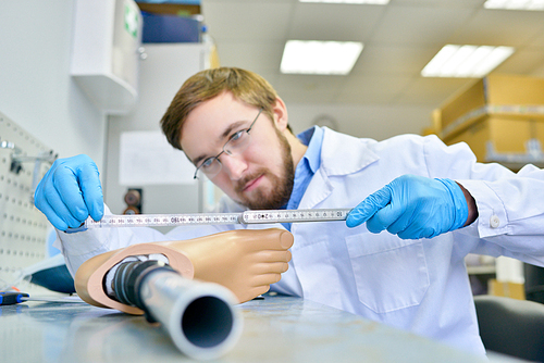 Portrait of prosthetist measuring artificial foot while working at table in design laboratory