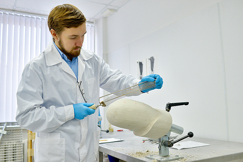 Portrait of young prosthetics technician sanding prosthesis molds while working in  modern design laboratory, copy space