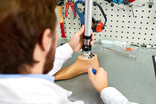 Over the shoulder view of young man assembling artificial foot sitting at table in modern laboratory