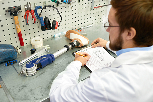 Prosthetics technician  making prosthetic leg at desk in office and writing notes on clipboard, copy space