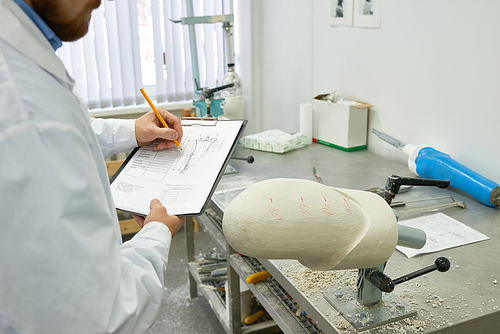 Portrait of young prosthetics technician  writing notes on clipboard while checking prosthesis molds in design laboratory, copy space