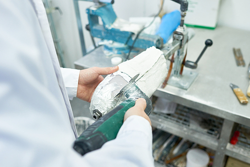 Close up of unrecognizable prosthetist working in design laboratory shaping leg part molds, copy space