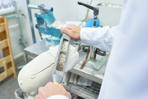 Close up of unrecognizable prosthetist working in design laboratory shaping and grinding leg part molds