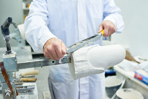 Front view mid-section  of unrecognizable prosthetist working in design laboratory shaping and grinding leg part molds