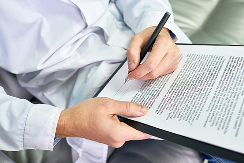 Close up of unrecognizable doctor signing form sitting in chair