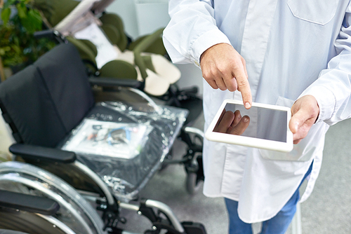 Close up of doctor using digital tablet with blank screen while standing by armchairs in hall of modern clinic