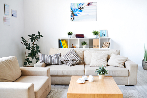 Modern interior of living room with abstract picture and certificates in frames on walls: comfortable sofa and armchair near coffee table